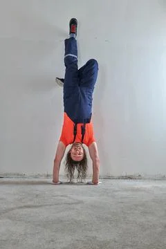 Cool construction worker in orange t-shirt stands upside down Stock Photos