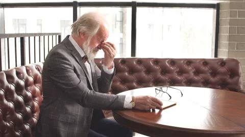 A cool gray- haired old man with a beard and a nice suit is sitting at a Desk in Stock Photos