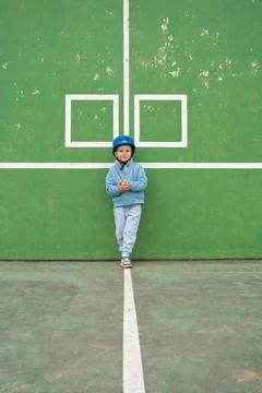 Cool kid posing on a playground, wearing a blue helmet and casual outfit. Green Foto stock
