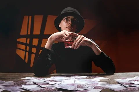 A cool man in dark glasses at a table with money and alcohol 写真素材