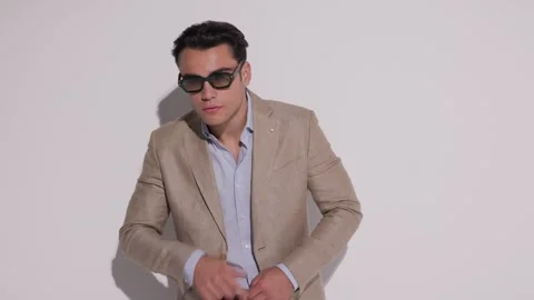 Cool man fixing sunglasses, buttoning beige jacket and placing hand in pocket 動画素材 327069921