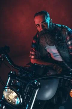 Cool man with long gray beard on motorcycle at night. Stock Photos