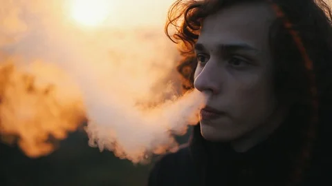 Cool portrait of vaping young man  outdoors at sunset.Closeup 動画素材 98749671