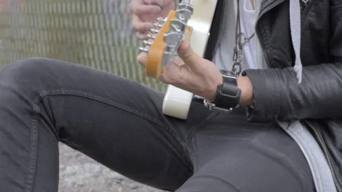 Cool rock guy playing the electric guitar by a steel fence Stock Footage 107084342