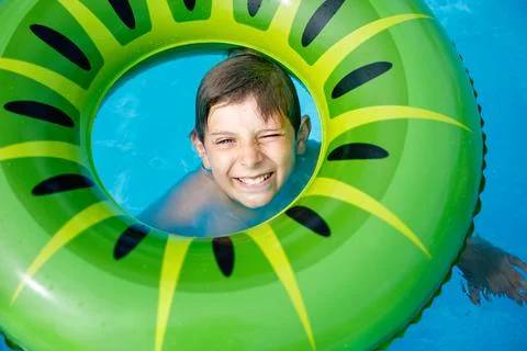 Cool school boy having fun on inflatable rubber circle in outdoor pool. Summer Stock Photos