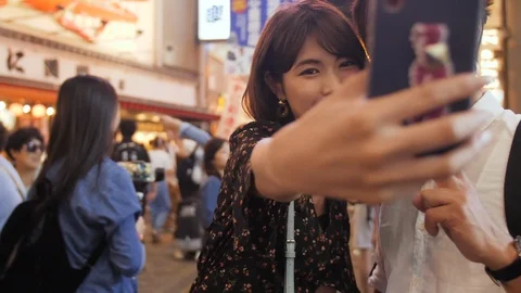 Cool young couple in 20's taking photos at Osaka night streets selfie togethe Stock Footage 111353211