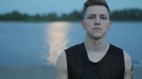 Cool young guy walking near the water on the embankment in the dusk, Slow motion Video stock 113066124