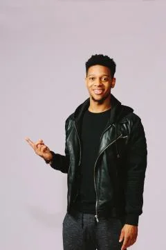 Cool young man pointing up at empty space with his index finger in a studio. Stock Photos