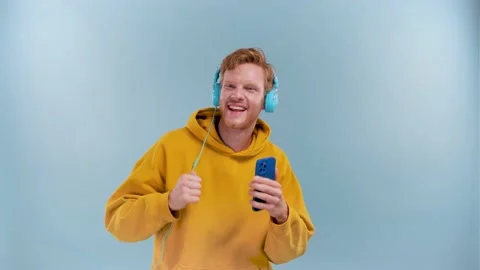 A cool young red-haired guy with headphones and a smartphone in his hands is Stock Footage 221769826
