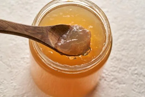 Cooled down congealed beef bone broth on a spoon and in a glass jar on a brig Stock Photos