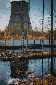 A cooling tower is visible behind trees and water Stock Photos