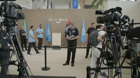 COP28, Dubai: Empty speaking desk surrounded by flags and cameras Stock Footage 289190446