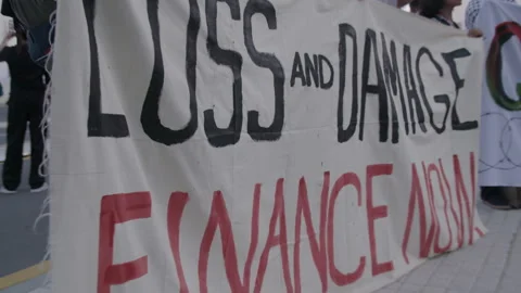COP28, Dubai: A protest flag with "Loss and Damage Finance Now" written on it Stock Footage 288449942