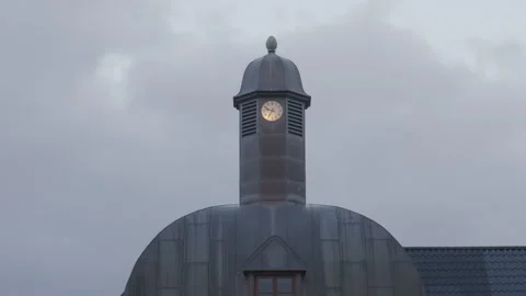 Copper clock tower with illuminated clock under cloudy sky during calm evening Stock Footage 311039425