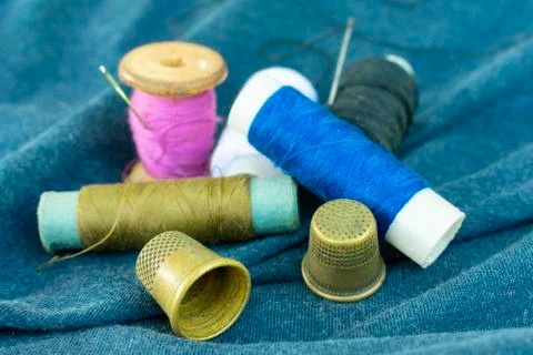 Copper old thimbles, colorful threads and needles on blue fabric, close-up Stockfoto's