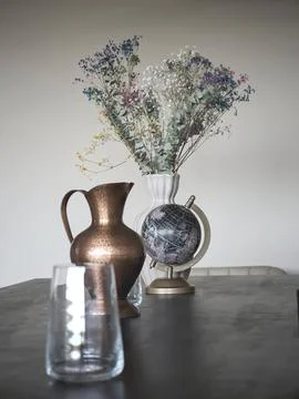 Copper pitcher, globe and dried flowers styled on dark dining table indoors Stock Photos