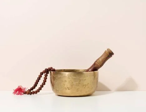 Copper singing bowl and wooden clapper on a white table. Musical instrumen... Stock Photos