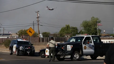 Cops at fire road block as planes drop red dust in background Stock Footage 114413317