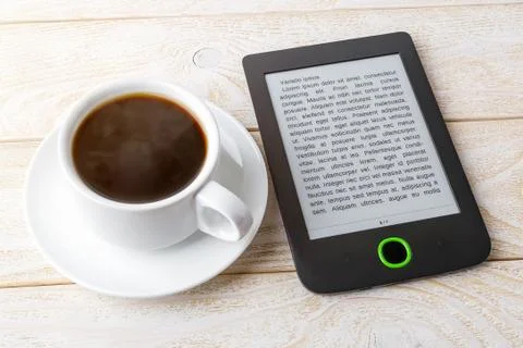 Copy space on a screen of e-book reader near cup of coffee on a wooden table Stock Photos