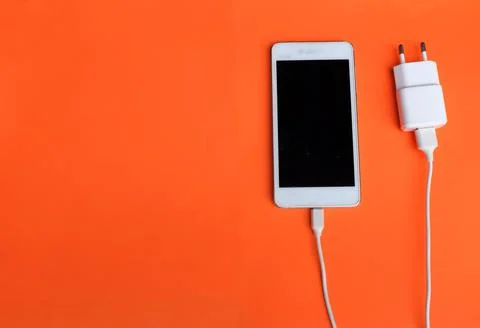 Copy space  white Smartphone Plug In with Charger Adapter on orange Background Stock Photos