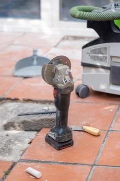 Cordless angle grinder stands beside a construction vacuum cleaner on tiled.. Stock Photos