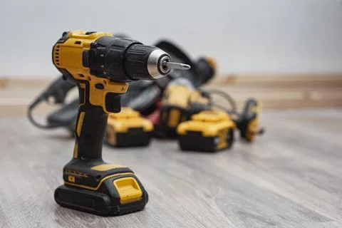 Cordless drill surrounded by various power tools on a wooden floor. Constru.. Stock Photos