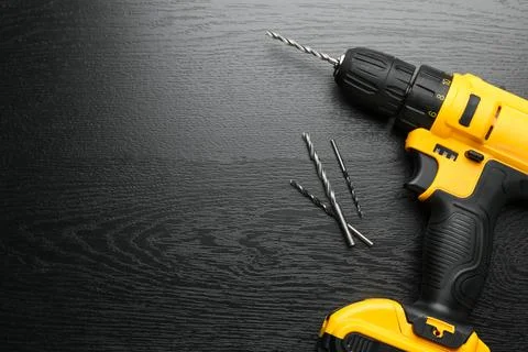 Cordless electric drill and bits on black wooden table, flat lay. Space for.. Stock Photos