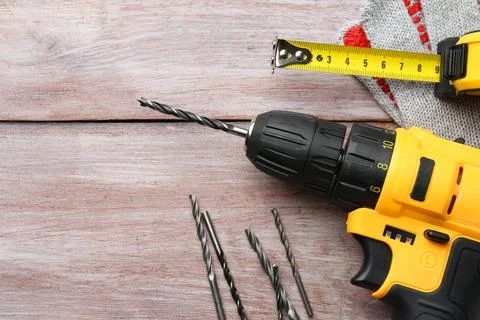 Cordless electric drill, bits and measuring tape on wooden table, flat lay... Stock Photos