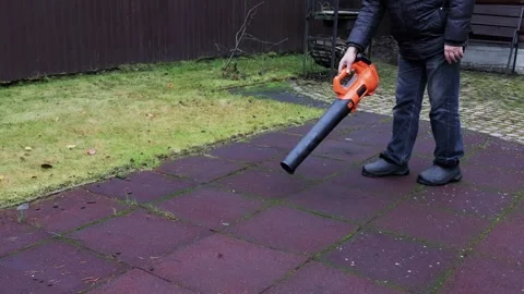 Cordless leaf blower clearing leaves from rubber play surface, front view Stock Footage 326967377