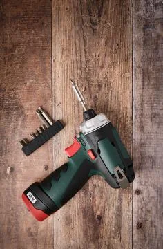 Cordless screwdriver drill and bit set lie on wooden table, professional tool Stock Photos