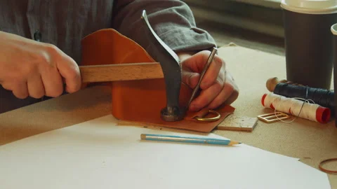 With a core and hammer, the tanner punches holes for sewing an exclusive bag Stock Footage 143732801