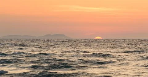 Corfu Sunset over the sea, in the background an island with an orange sun ove Stock Photos