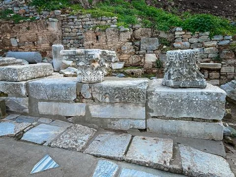 Corinthian Capitals Stack atop Marble Slabs Amid Ivy-Draped Walls 스톡 사진