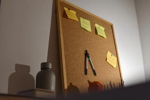 Cork board with yellow sticky notes, drawing compass, warm light, shadows Foto stock
