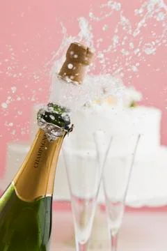 Cork exploding from champagne bottle with wedding cake in background Stock Photos