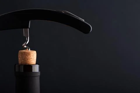 Corkscrew opening wine bottle with a cork on a dark background Stock Photos