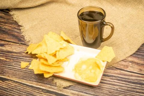 Corn chips with cheese sauce and a coffee mug on a wooden background. Close u Stock Photos