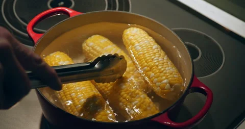 Corn on the cob boils on a stove top as a man stirs the pot. Video stock 131485283