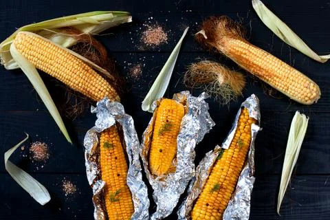 Corn on the cobs, baked in foil on the black wooden table, top view Stock Photos