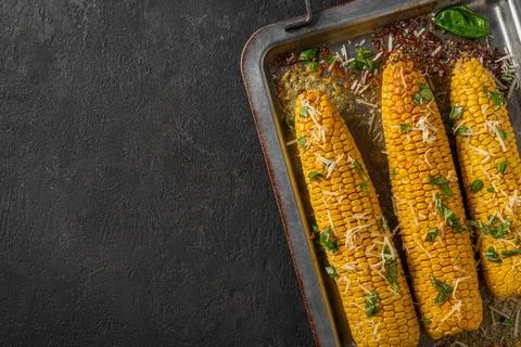 Corn cobs grilled and baked on baking sheet with parmesan cheese and basil... Stock Photos