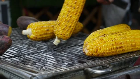 Corn cobs turn over a hot grill, their kernels popping and sizzling in the heat Stock Footage 312110368