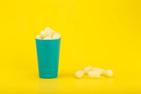 Corn curls in blue plastic cup with against yellow background with copy space Stock Photos
