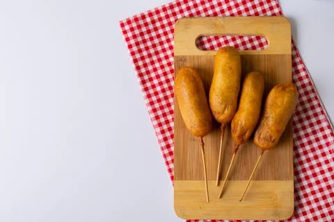 Corn dogs served on serving board with checked pattern napkin over white 스톡 사진