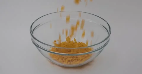 Corn flakes are poured into a glass bowl in slow motion on white background Stock Footage 148650719