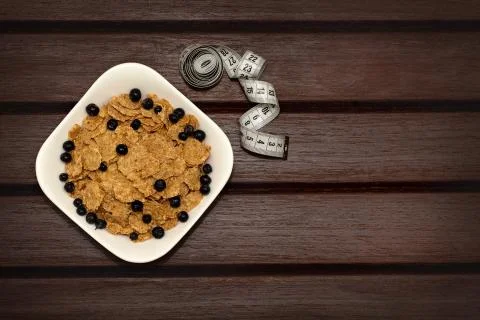 Corn flakes with berries in white plate on brown wooden boards. Stock Photos