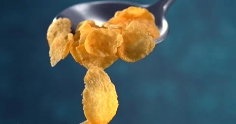 Corn flakes falling from a spoon in slow motion on blue background Stock Footage 346256041