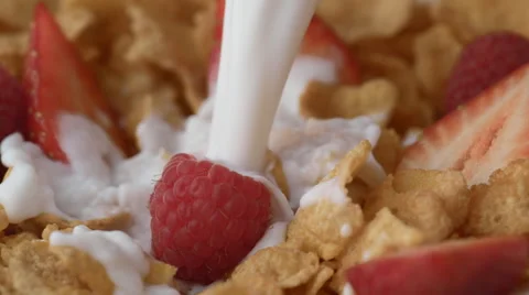 Corn flakes with raspberry and strawberry in a bowl pouring with milk. Slow Stock Footage 60964651