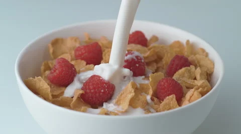 Corn flakes with raspberry in a bowl pouring with milk. Slow Motion. Stock Footage 60964622