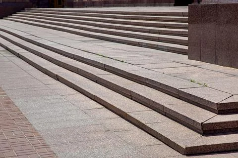 The corner of granite staircase with stone steps rise to building facade. Stock Photos