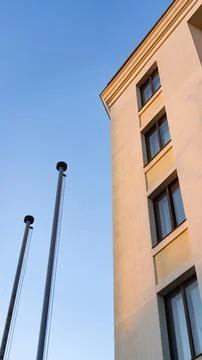 Corner of an orange building, flagpoles on the left, against a clear, blue sk Stock Photos
